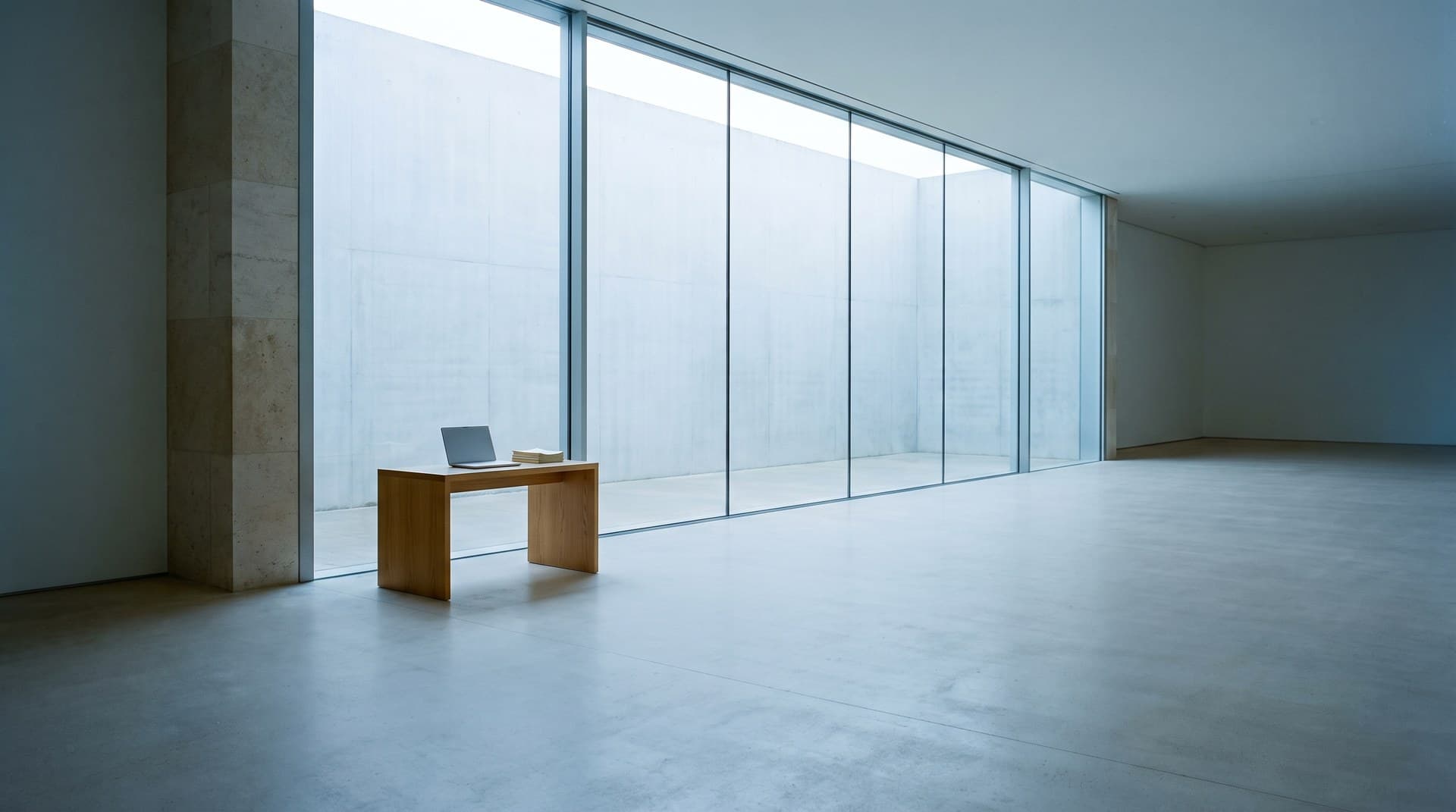 An enormous floor-to-ceiling glass window wall in a bare concrete room with one small desk beside it, a physical metaphor for Claude's 1M token context window being far larger than most agent tasks need