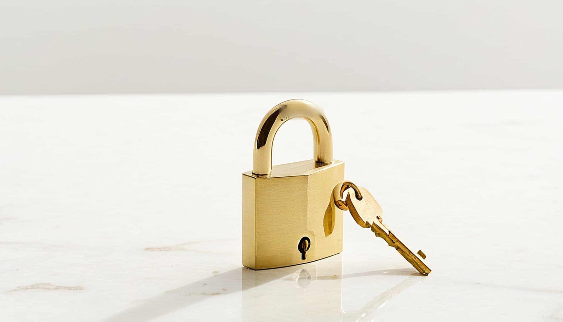 A brass padlock resting beside its key on white marble, representing n8n Git source control locked behind a paid plan